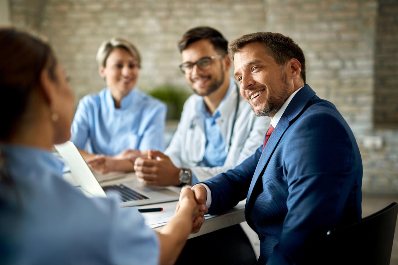 happy-businessman-having-meeting-with-group-doctors-shaking-hands-with-one-them-office